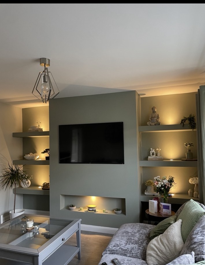 Finished sage-green media wall with illuminated shelving and furnished living room